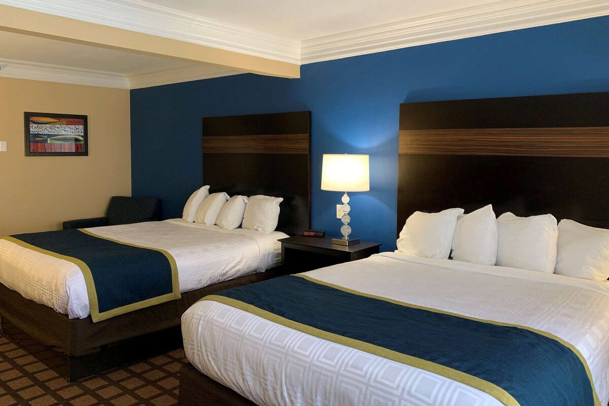 A hotel room with two beds, a nightstand with a lamp, and a wall-mounted painting.