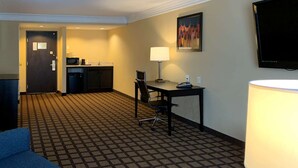 A hotel room with a checkered carpet, a desk with a chair, a television mounted on the wall, and a door leading to a kitchenette. - Comfort Inn Saint Paul East (Oakdale)