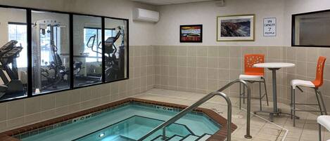 A small indoor pool with a tiled floor, exercise equipment, and a seating area with two tables and chairs.