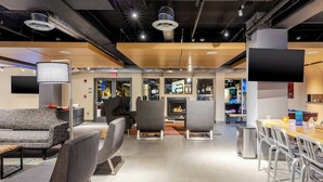 A modern lounge area with seating, a fireplace, and a large TV screen. - Aloft by Marriott Columbia Harbison (Columbia)