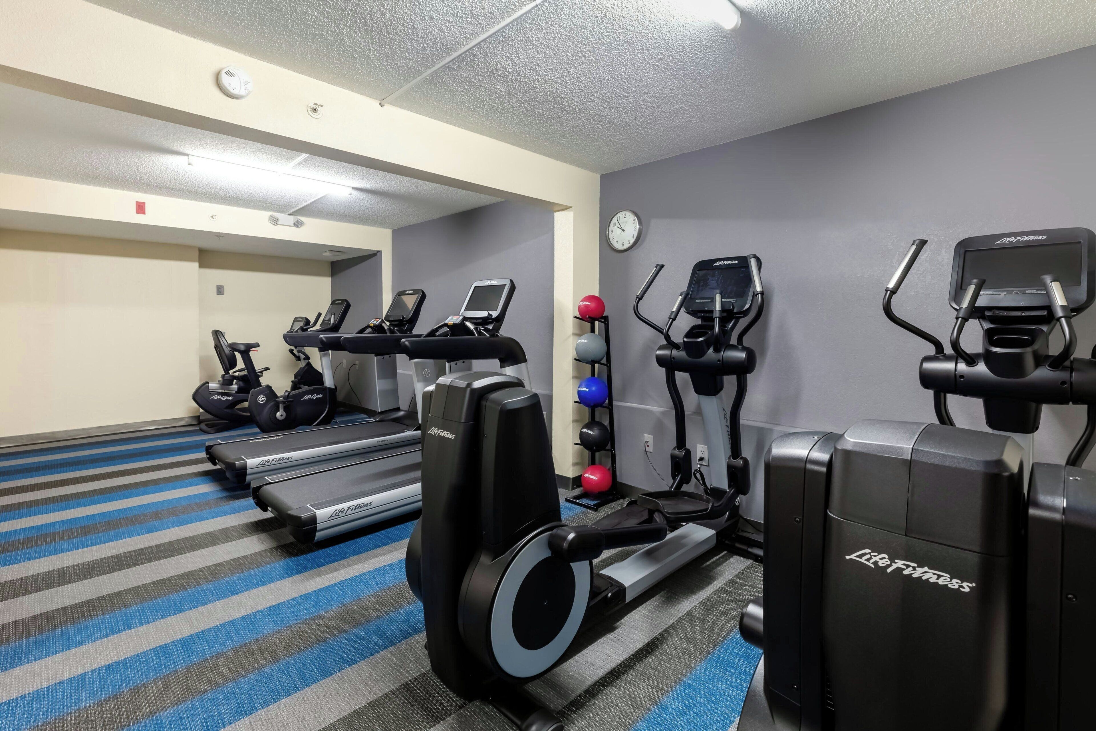 Un gimnasio con cintas de correr, elípticas y una bicicleta estática de pared.