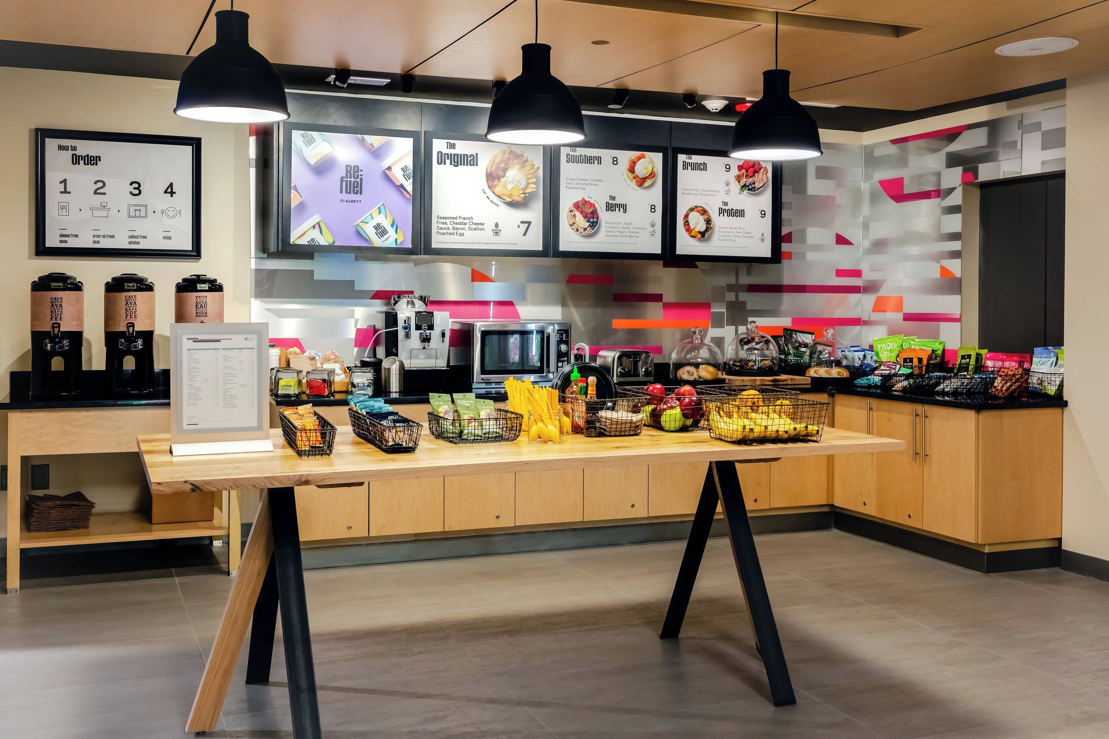 Un caffè moderno con un bancone in legno, luci a sospensione nere e lavagne che mostrano diverse proposte gastronomiche.