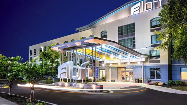 A modern hotel with a prominent 'aloft' sign, a covered entrance, and a landscaped area with trees. - Aloft by Marriott Columbia Harbison (Columbia)