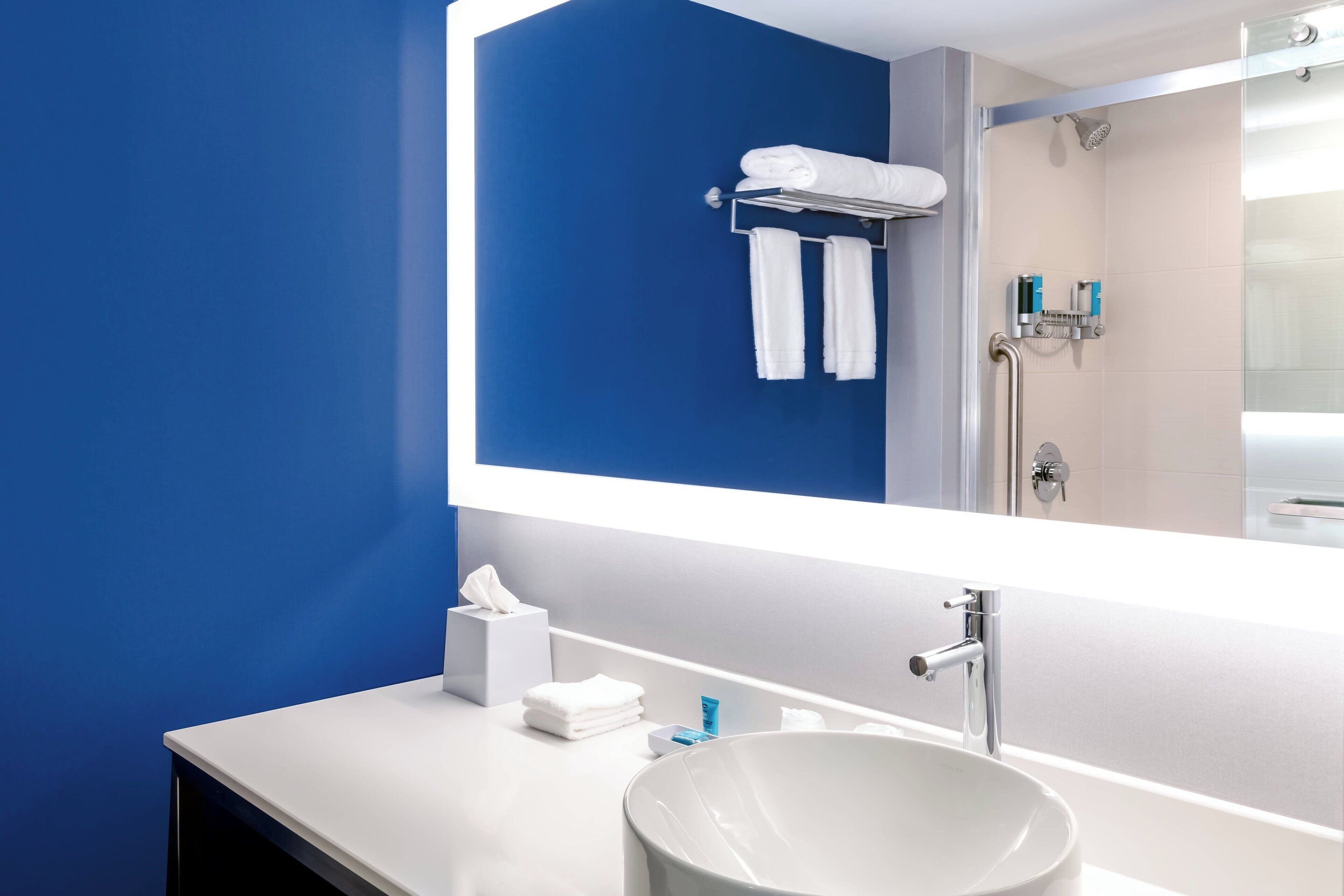 A modern bathroom with a large mirror, white sink, and blue walls.