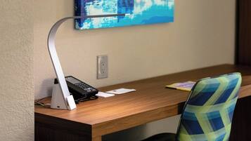 A wooden desk with a white desk lamp, a black phone, and a blue patterned chair.