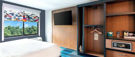 Una camera d'albergo con un letto, un'ampia finestra vista verde, una TV a parete e un armadio a muro con pannello di controllo.