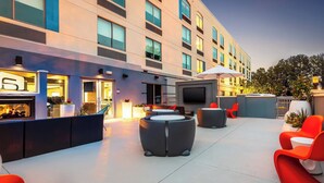 A modern outdoor lounge area with seating and a TV screen, surrounded by a building with large windows and a flat facade. - Aloft by Marriott Columbia Harbison (Columbia)