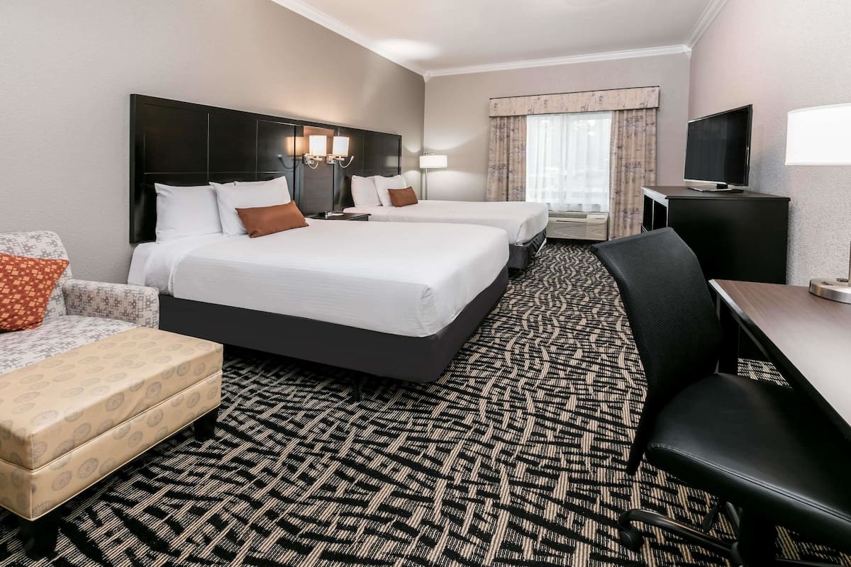 A hotel room with two beds, a desk, a TV, and a patterned carpet.