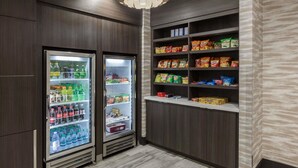 En tekøkken med to køleskabe fyldt med drikkevarer og snacks, samt hylder med emballerede fødevarer.