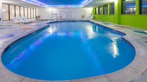 En indendørs swimmingpool med krystalklart vand, omgivet af liggestole og en flisebelagt terrasse.