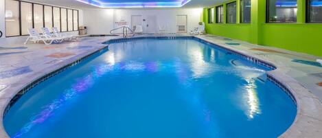 An indoor swimming pool with clear water, surrounded by lounge chairs and a tiled deck.