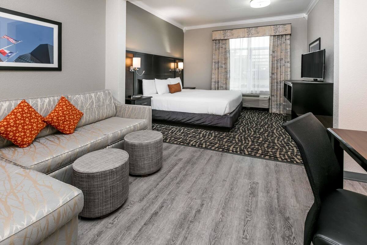 A hotel room with a bed, a sofa, two ottomans, a desk, and a TV.