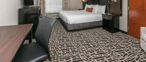 Una habitación de hotel con cama, mesita de noche, lámpara, televisor y alfombra estampada.