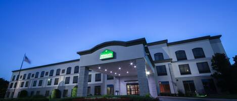 A hotel with a prominent green sign, multiple floors, and a well-lit entrance.