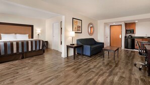Quarto de hotel com cama, sofá, mesa pequena, escrivaninha e cozinha compacta.