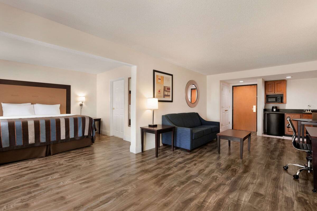 A hotel room with a bed, a sofa, a small table, a desk, and a kitchenette.