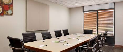 Un salón de conferencias con una larga mesa, sillas negras y una pizarra.