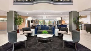 Um hall amplo com design moderno, com área de estar central com sofás e poltronas, mesa de centro e plantas em vasos.