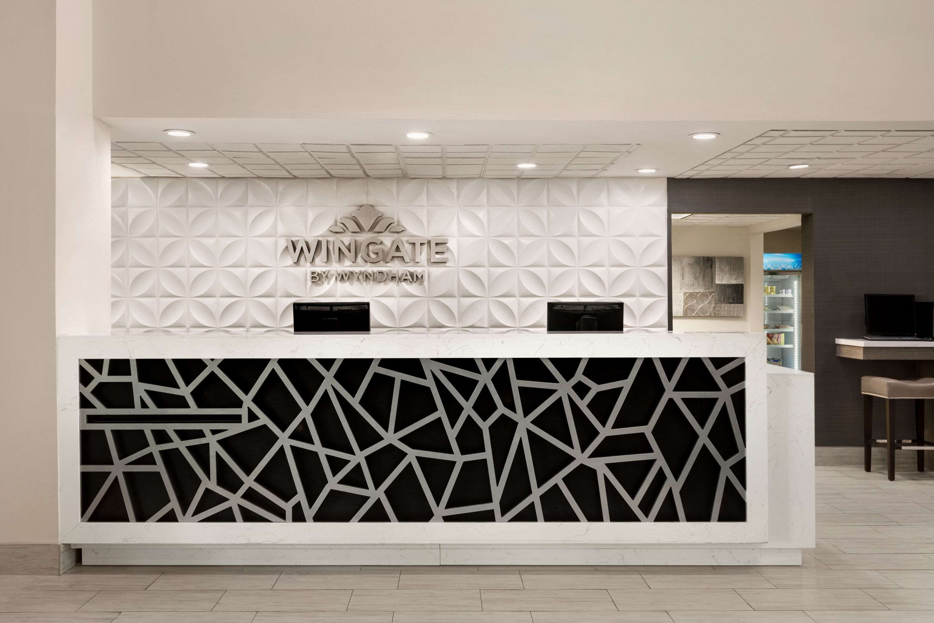 Balcão de recepção com padrão geométrico e a inscrição "Wingate by Wyndham" na parede.