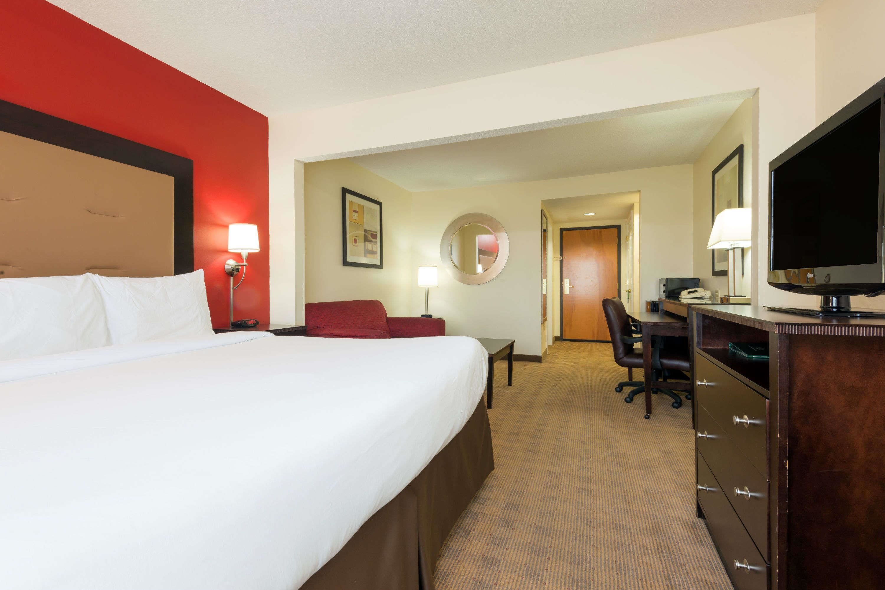 Quarto de hotel com uma cama grande, uma escrivaninha, uma cadeira, uma televisão e um espelho.