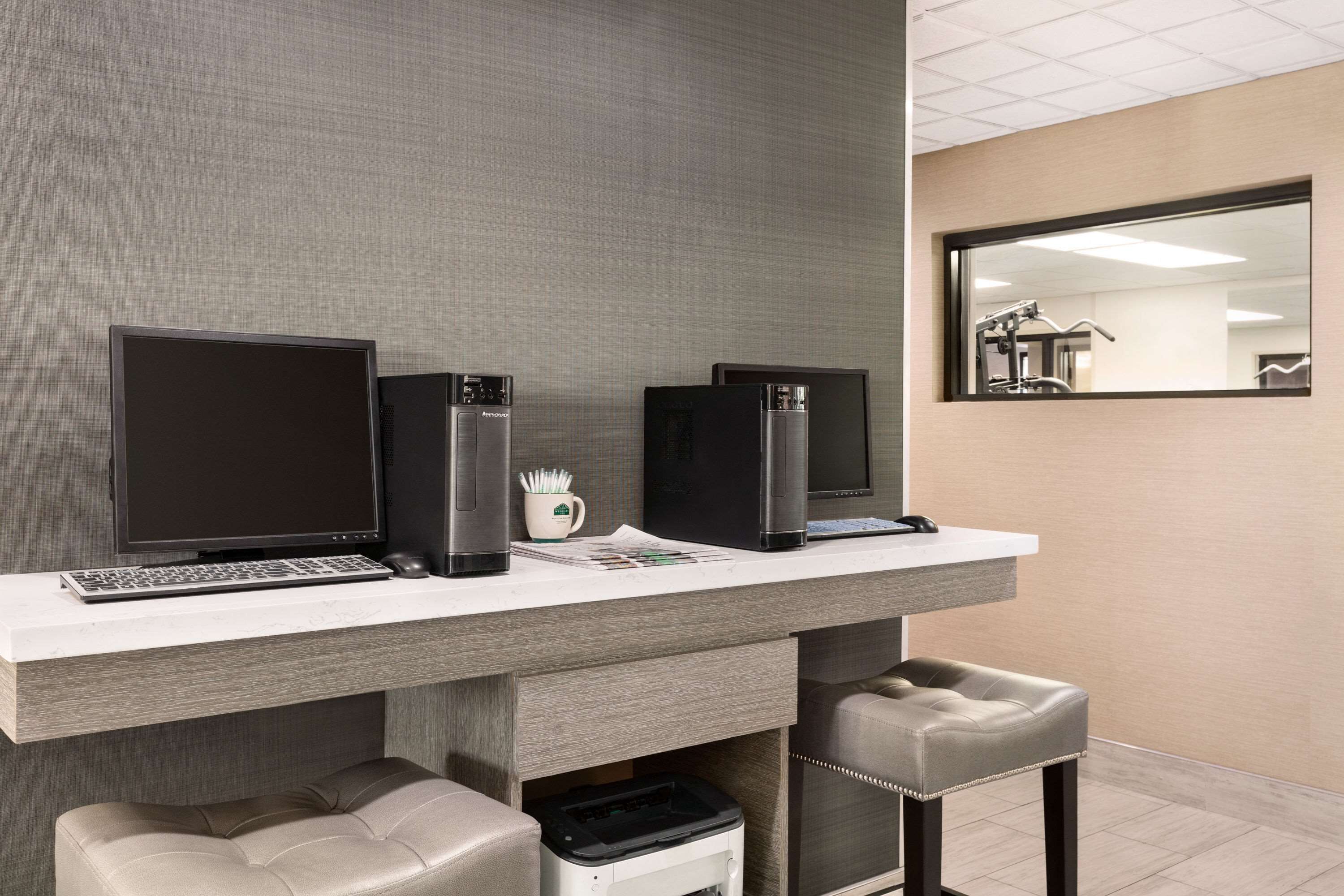 A modern office space with a desk, two monitors, a keyboard, a printer, and a coffee cup.