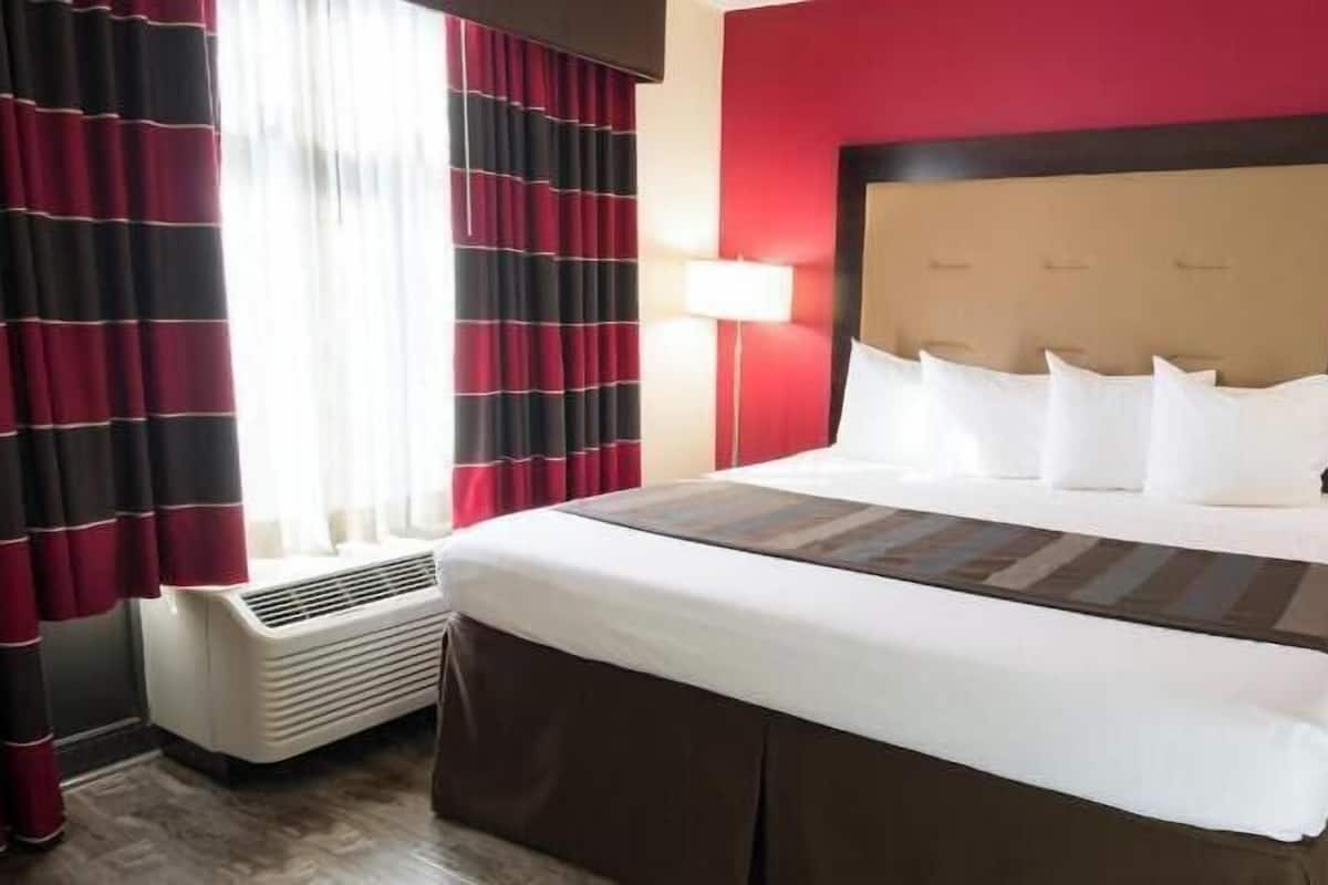 A hotel room with a large bed, red walls, and a window with curtains.