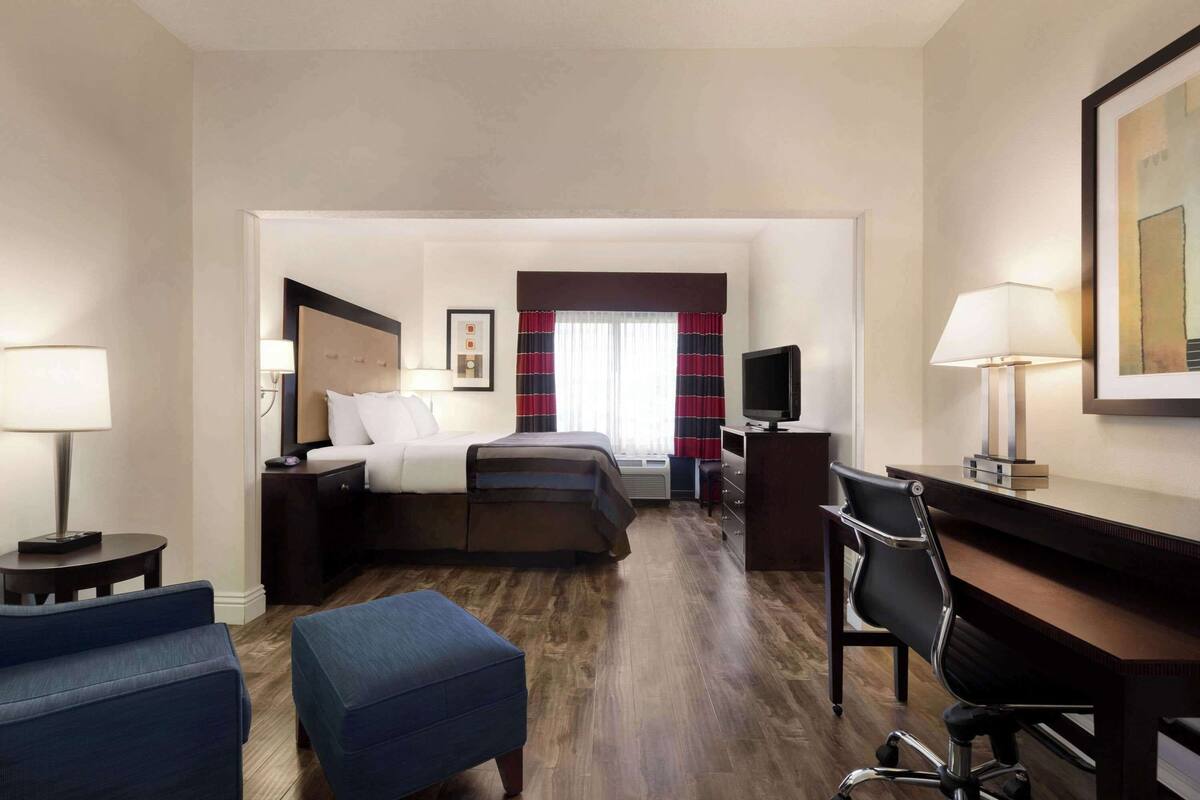 A hotel room with a bed, a desk, a chair, a TV, and a lamp.