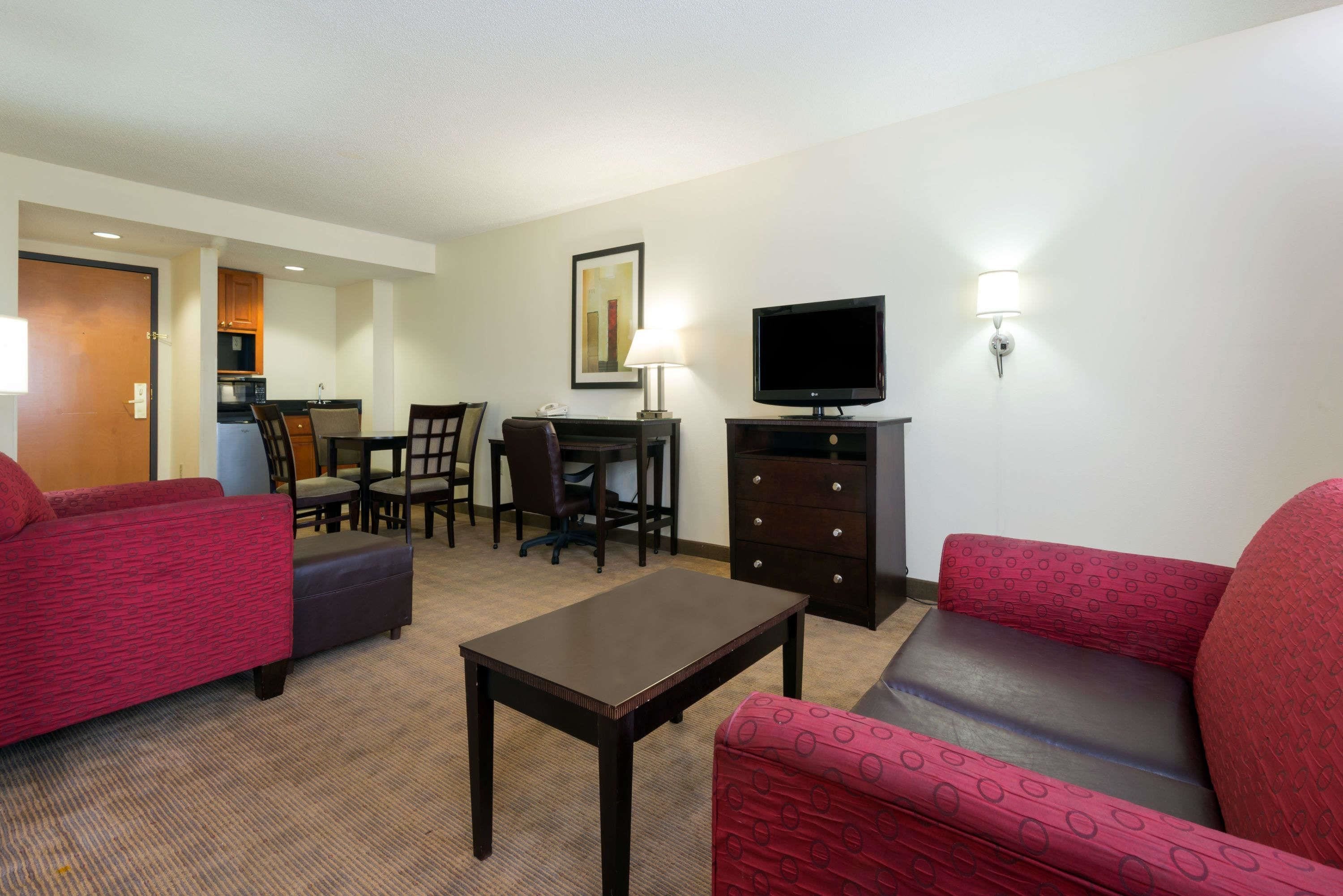 A hotel room with a red sofa, a small table, a TV, a lamp, and a desk with chairs.