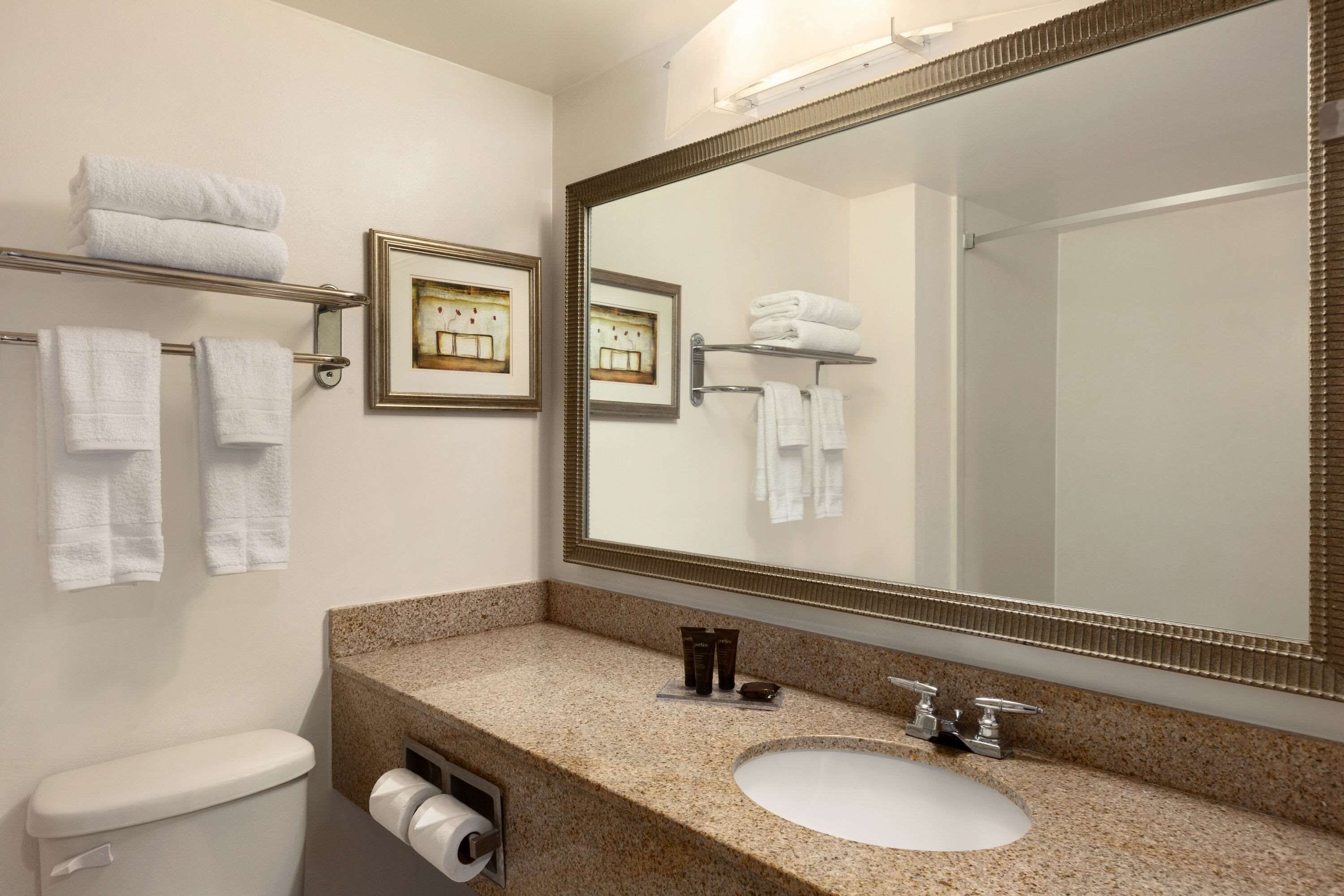 A bathroom with a white toilet, a sink with a large mirror, and multiple towel racks with folded towels.