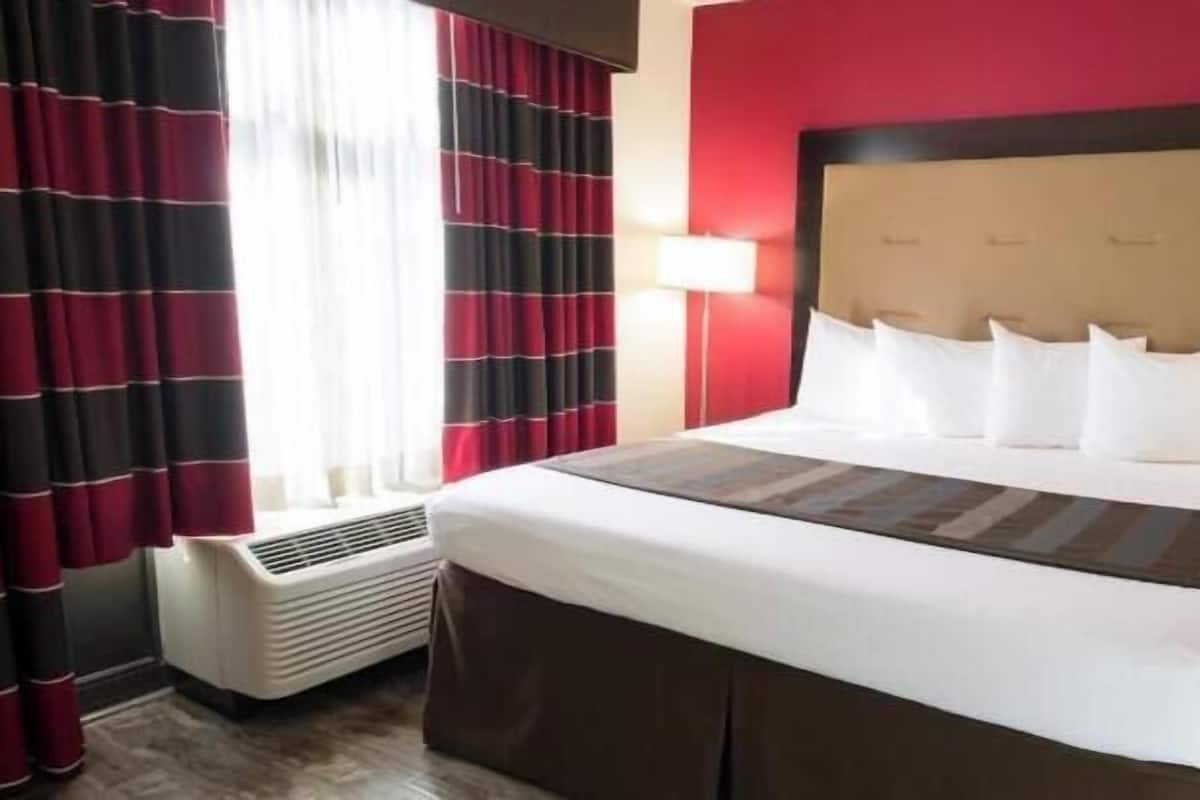 A hotel room with a large bed, red walls, and a window with curtains.