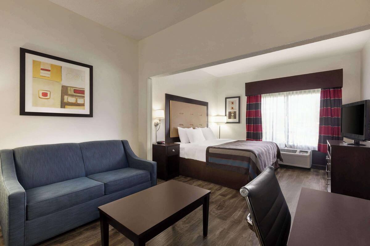 A hotel room with a bed, a sofa, a desk, a TV, and a window with curtains.