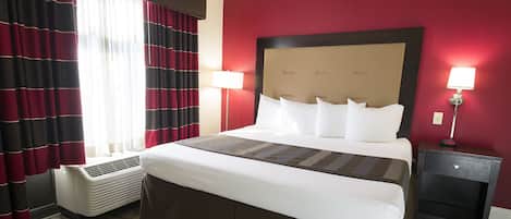 A hotel room with a large bed, two bedside lamps, a heater, and a nightstand with a lamp.