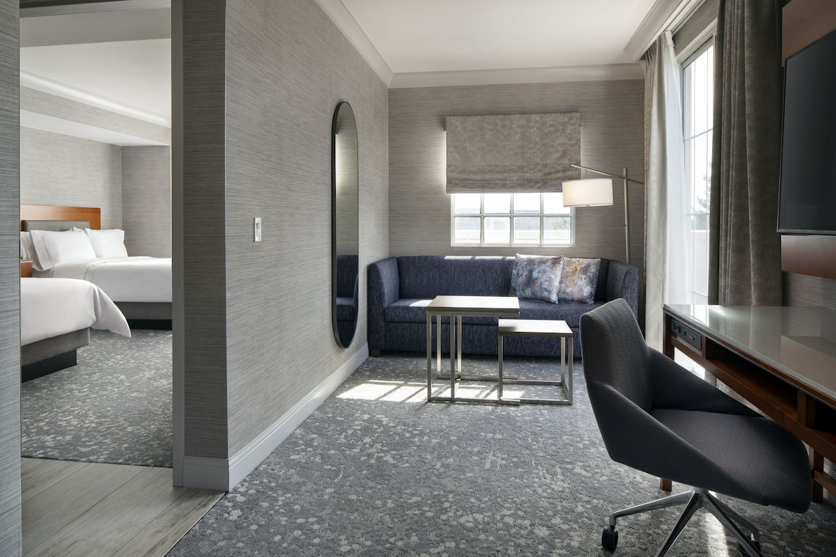 A modern hotel room with a bed, a sofa, a desk, and a TV.