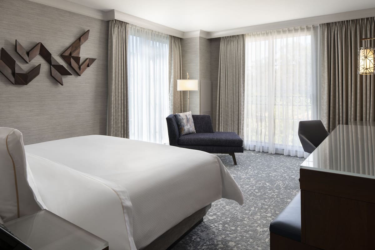 A hotel room with a large bed, a desk, a chair, and a lamp.