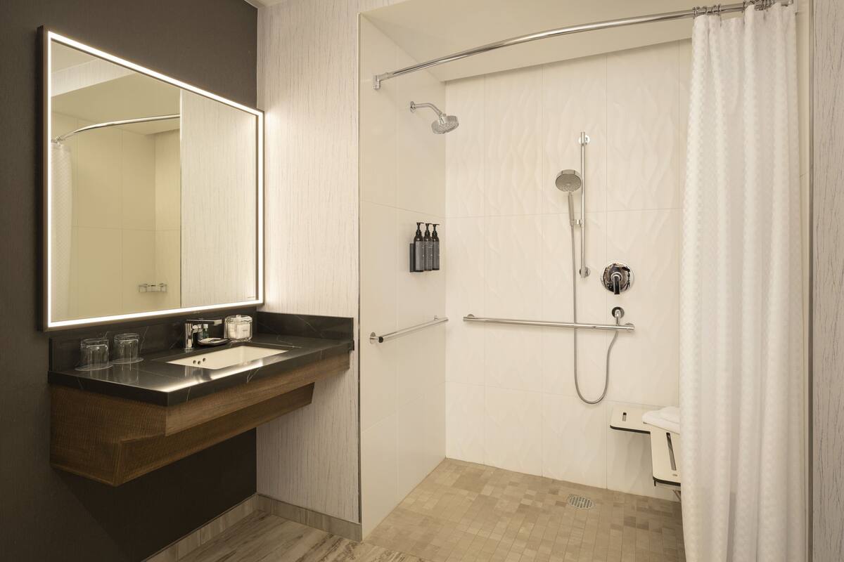 A modern bathroom with a large mirror, a sink, a shower with a glass door, and a toilet.