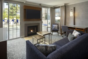 A modern living room with a fireplace, seating area, and large windows offering a view of the outdoors.