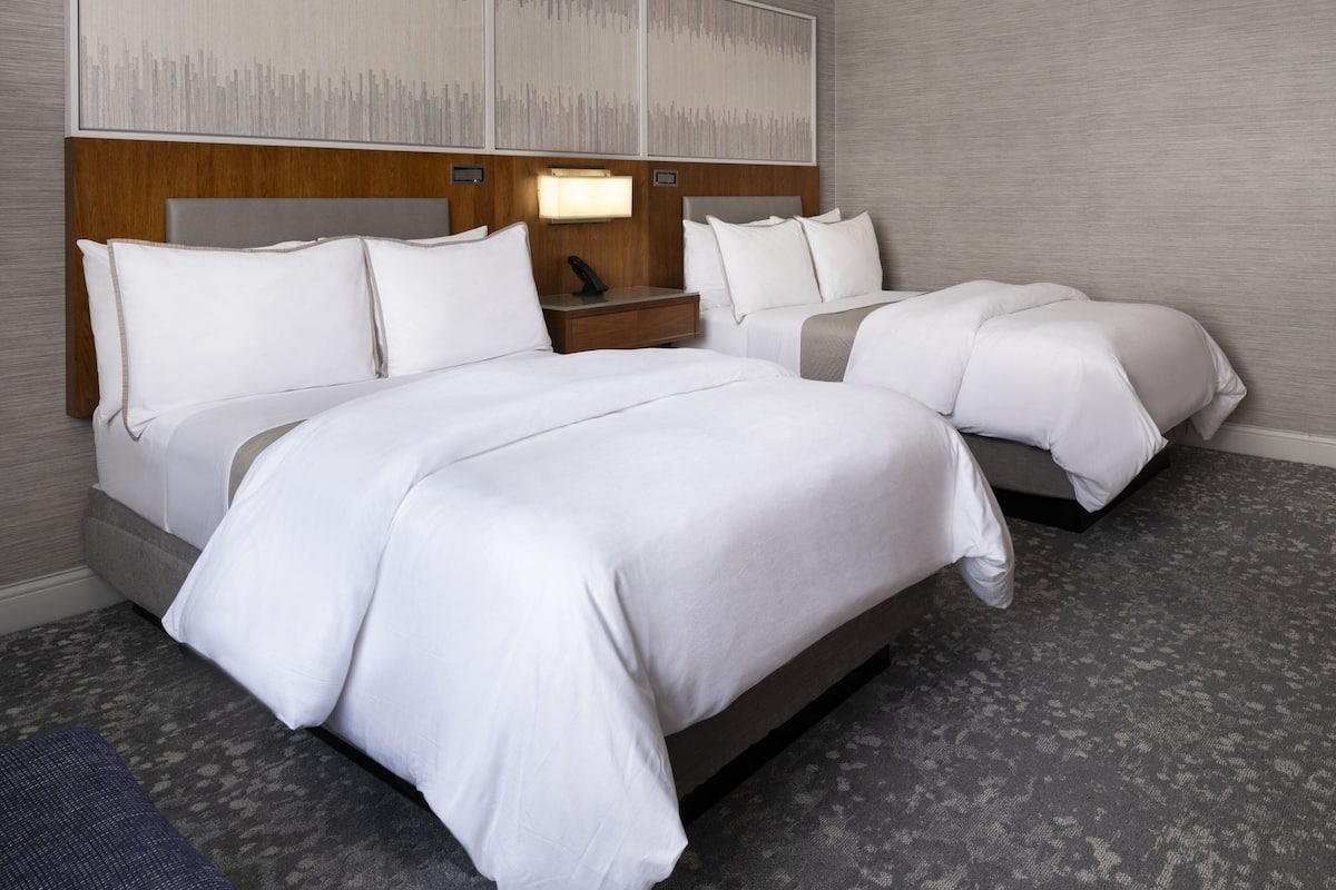 A hotel room with a large bed, a bedside table, a lamp, and a headboard with a cityscape mural.