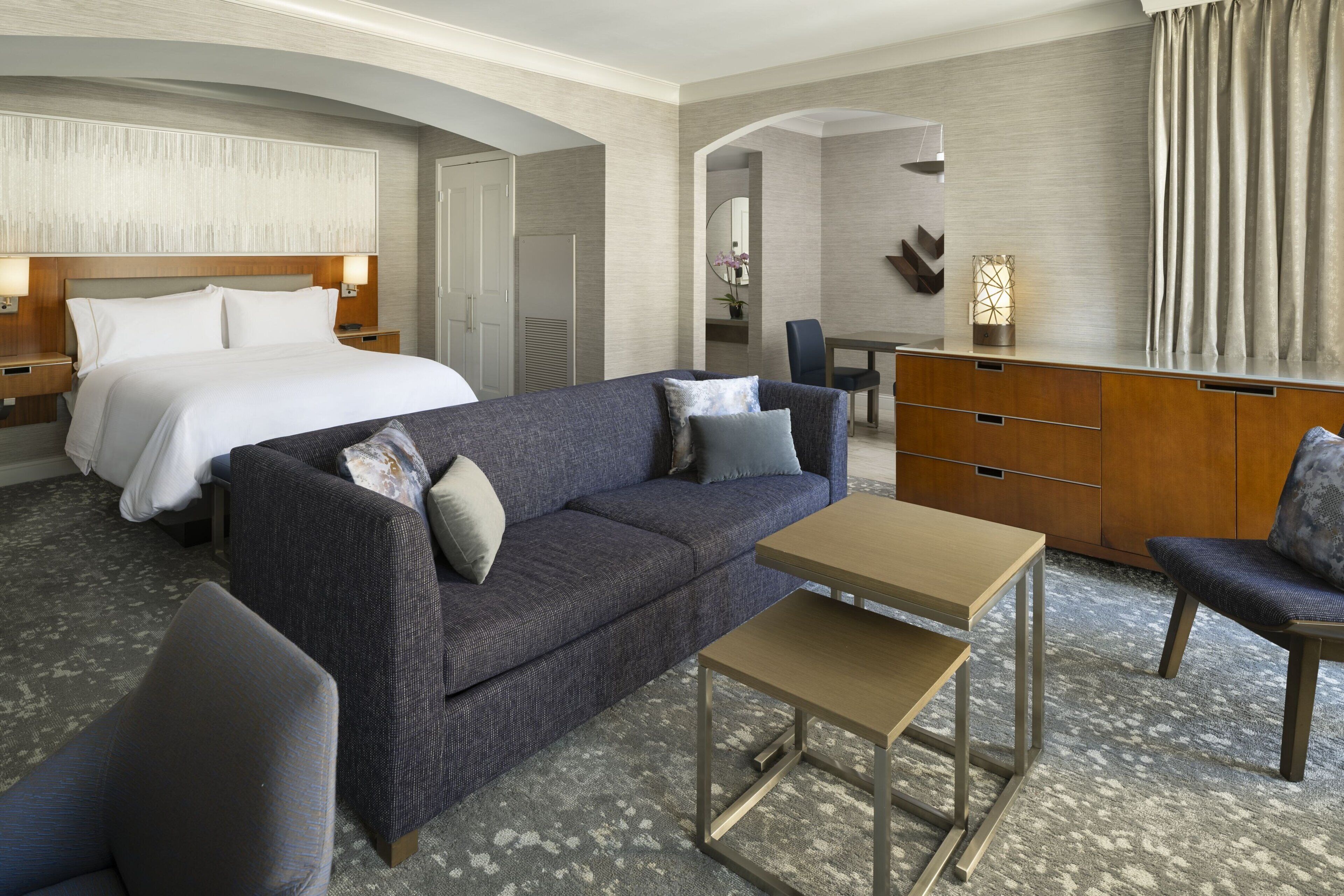 A hotel room with a bed, a sofa, a coffee table, a desk, and a dresser.
