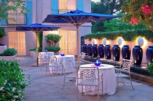 An outdoor patio with round tables and chairs, umbrellas, and decorative vases.