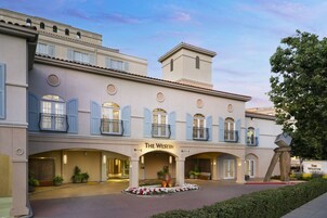 Un hotel con fachada clásica, varios balcones y una entrada central con un macizo de flores.