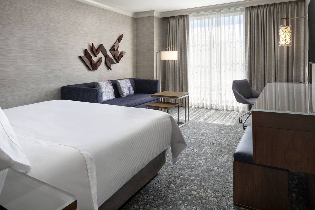 A modern hotel room with a large bed, a sofa, a desk, and a chair.