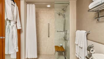 A modern bathroom with a glass shower enclosure, a wooden stool, and a towel rack.