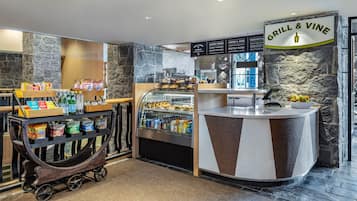 A restaurant counter with a stone wall backdrop, a menu board, and a variety of food and drink items on display.