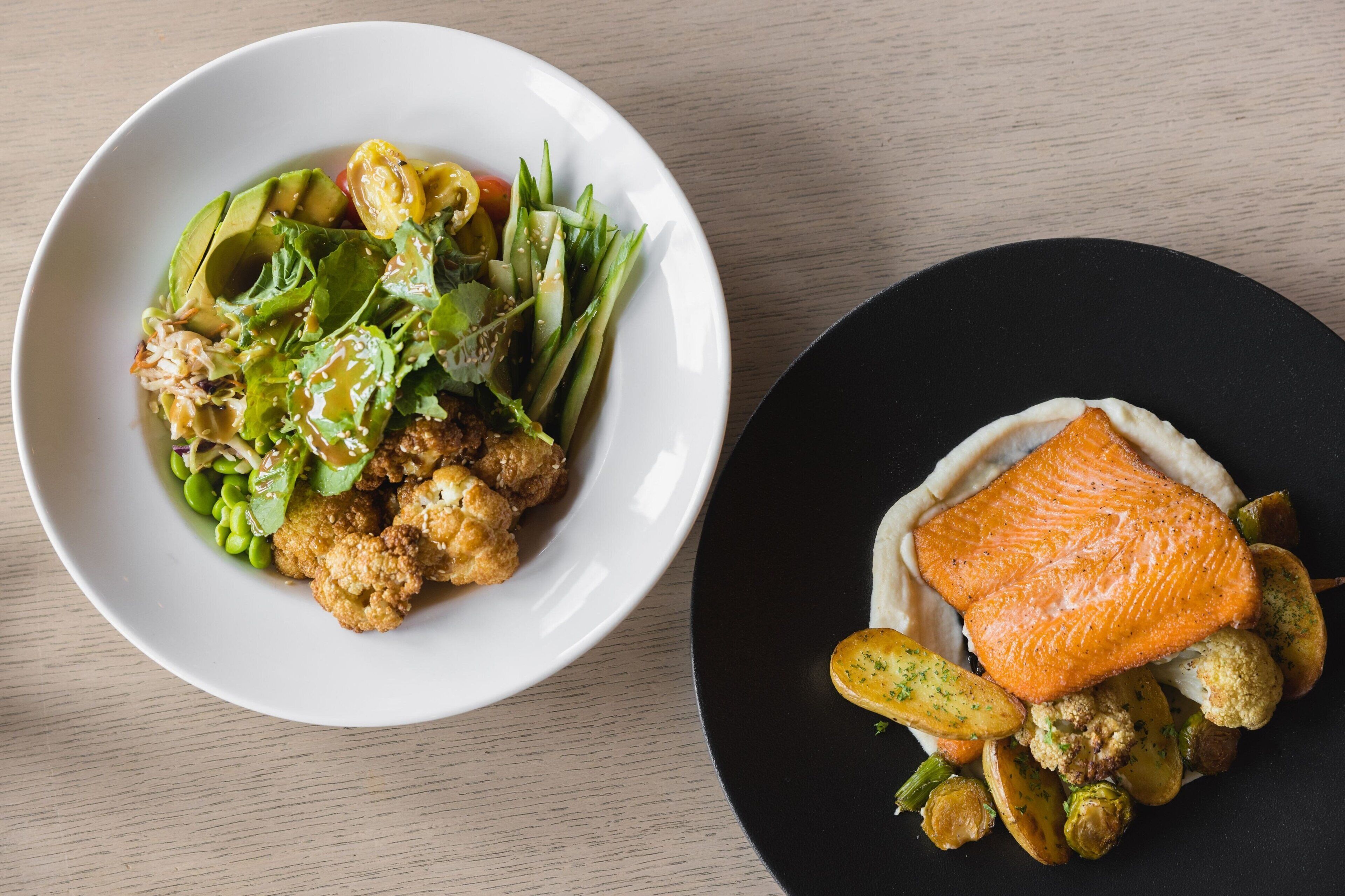Zwei Teller Essen, einer mit Salat und der andere mit Lachs und Gemüse.