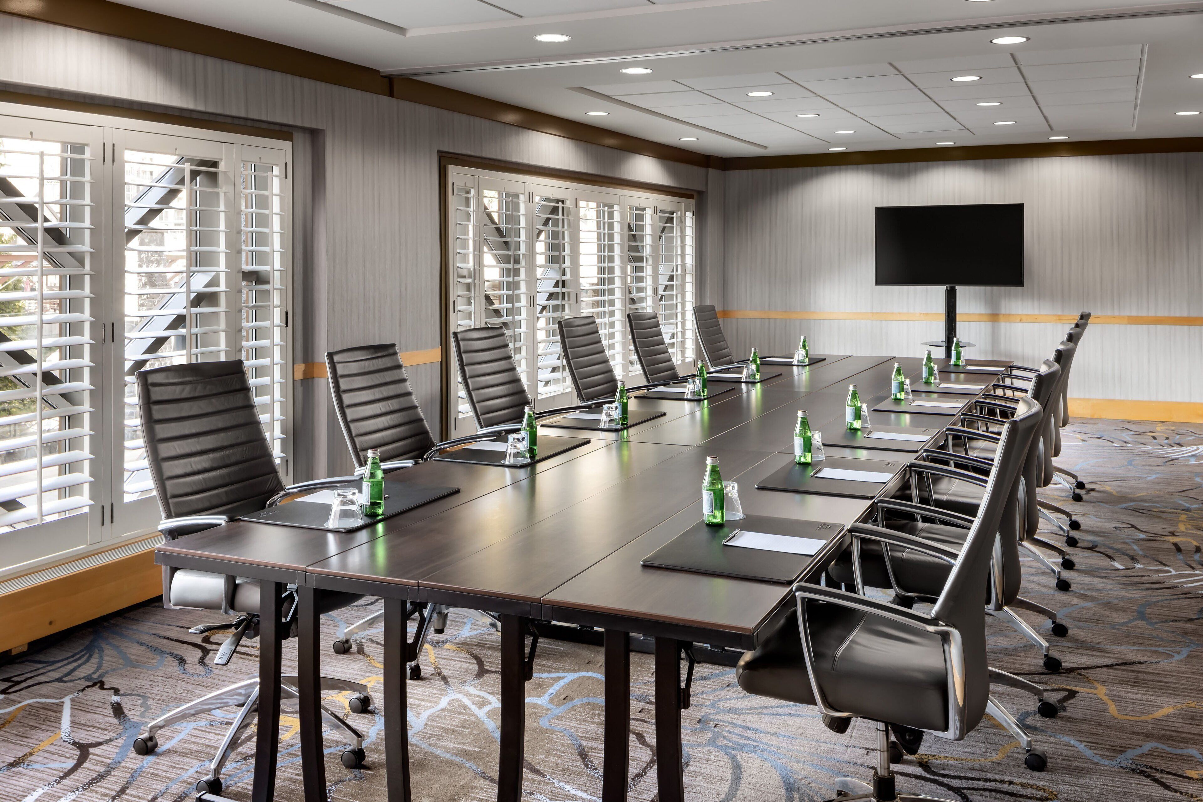 A conference room with a long table, multiple chairs, and a flat-screen TV on the wall.