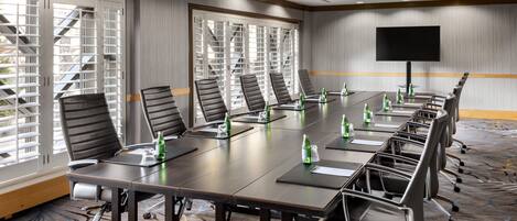 A conference room with a long table, multiple chairs, and a flat-screen TV on the wall.
