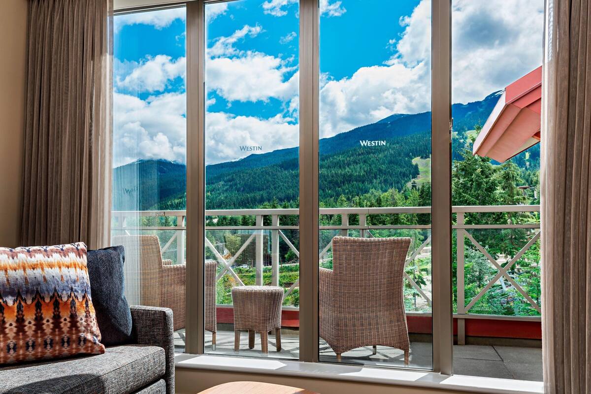 A balcony with wicker furniture, a view of a mountainous landscape, and the word "WESTIN" on the glass.