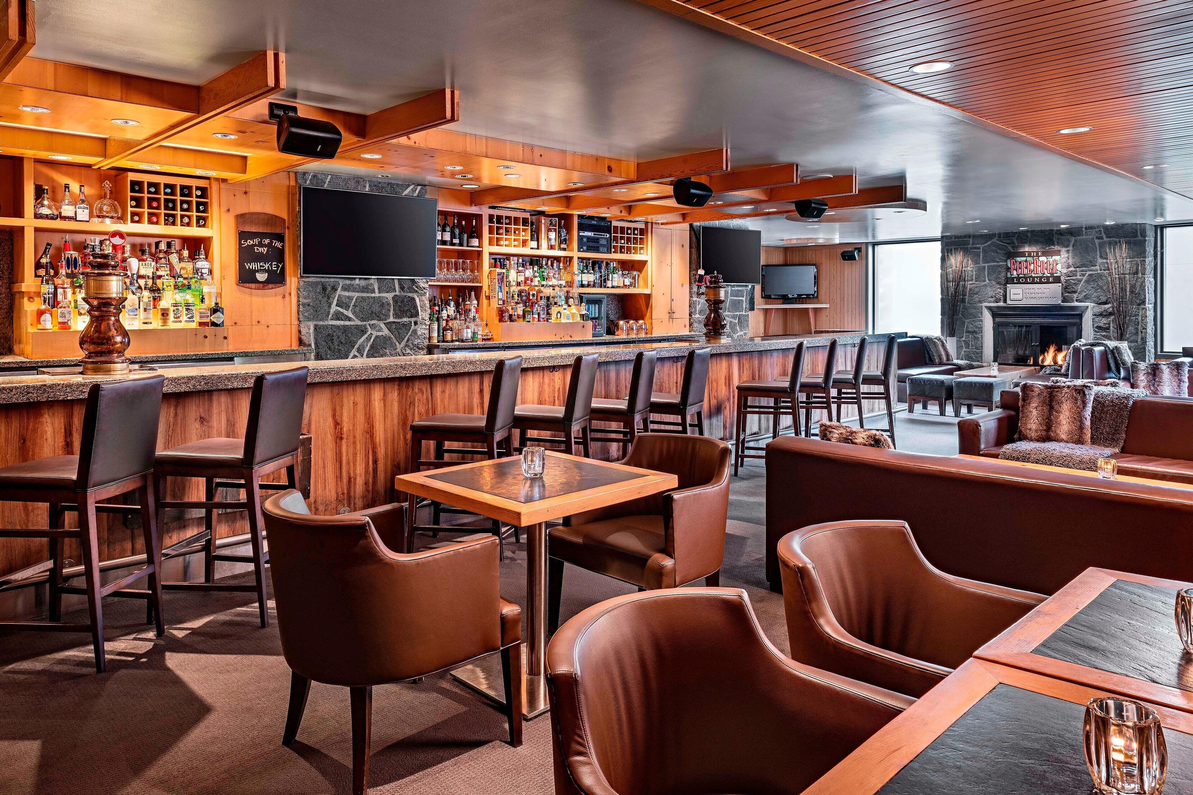 A bar area with wooden shelves stocked with liquor, leather seating, and a stone fireplace.