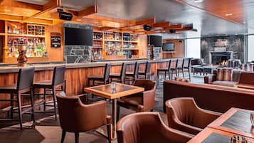 A bar area with wooden shelves stocked with liquor, leather seating, and a stone fireplace.