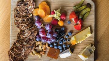 A wooden board with sliced bread, fruits, nuts, and cheese.